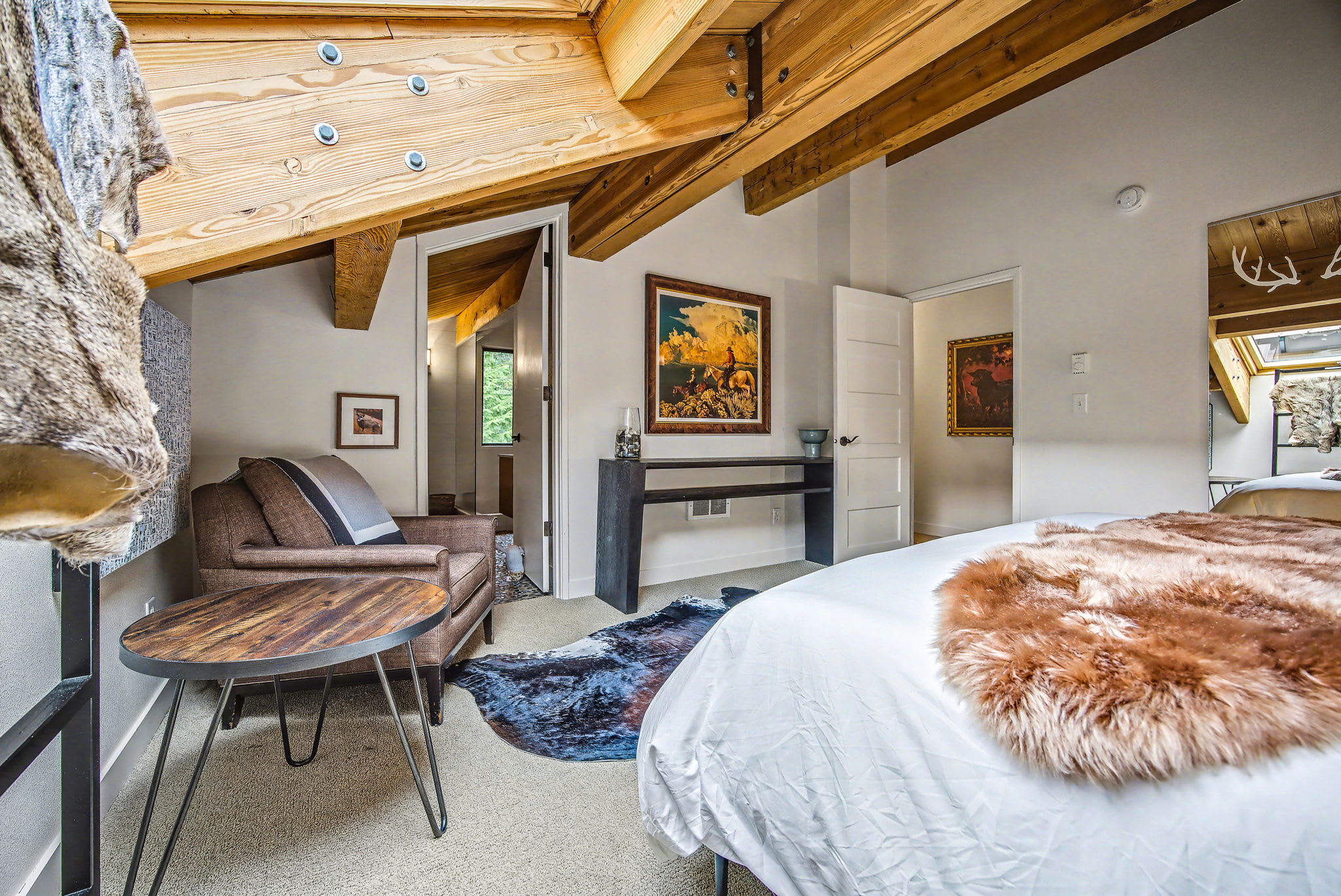 Cozy corner of the living room featuring a console table with decorative items and framed artwork on the wall. Large windows provide ample natural light and immersive forest views.