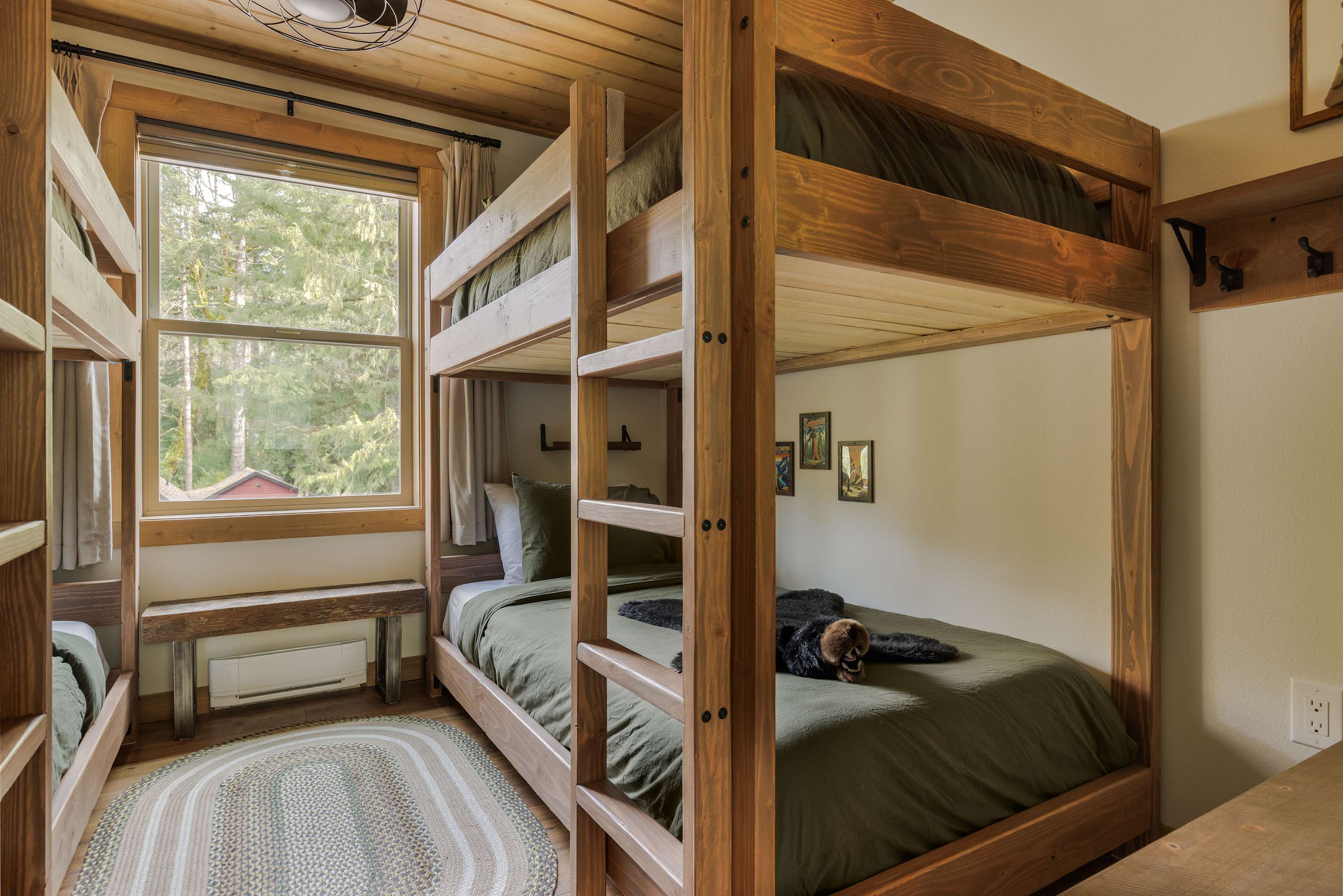 Another view of the bunk room, highlighting a wooden bunk bed with dark green bedding and a plush bear toy. A large window provides natural light and a view of the outdoors.