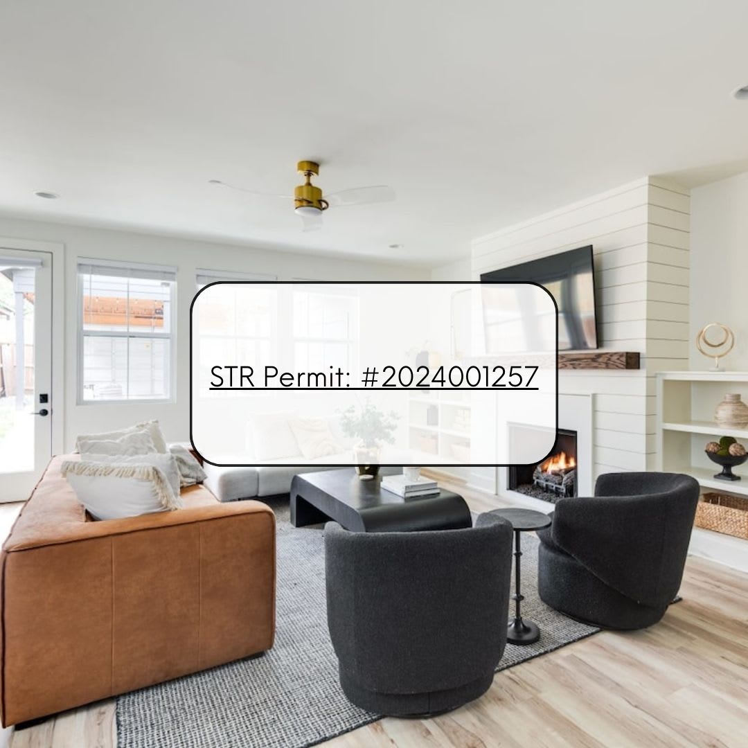A bright living room with light wood floors, a brown leather sofa, two dark gray armchairs, and a white shiplap fireplace, overlaid with a white box displaying an STR permit number.