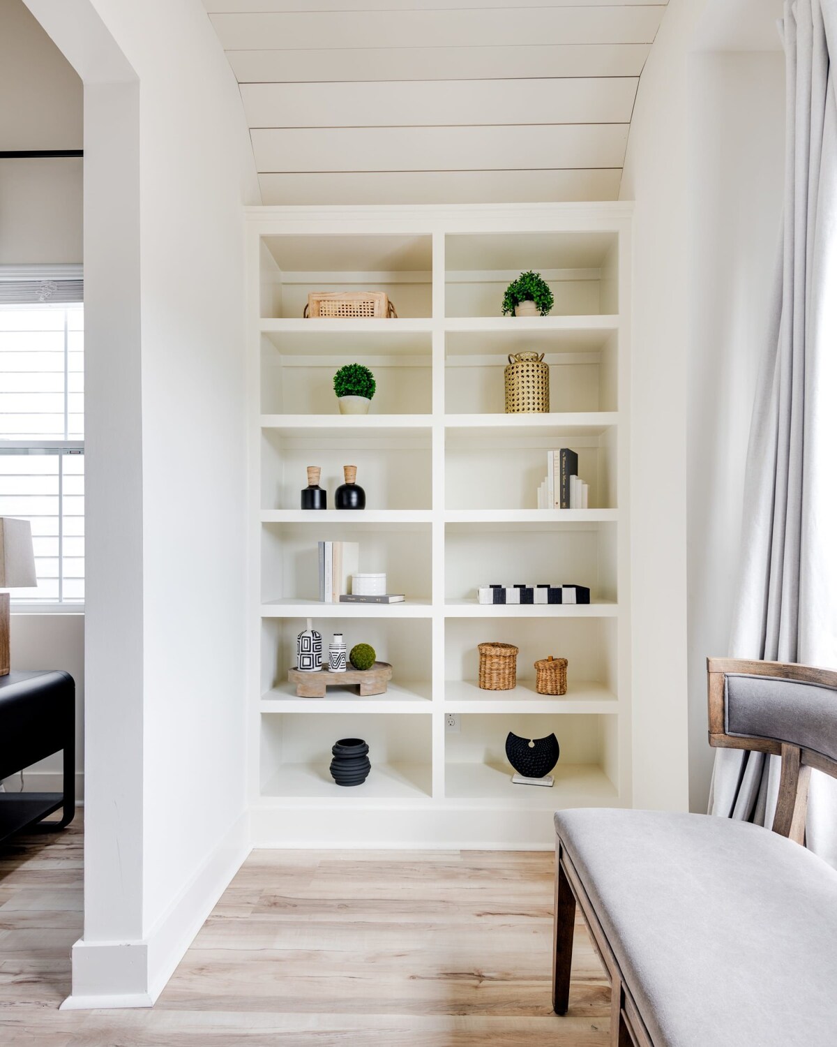 A stylish built-in bookshelf filled with an assortment of decorative objects, including small plants, woven baskets, books, and abstract sculptures, adding texture and visual interest to the room's design.