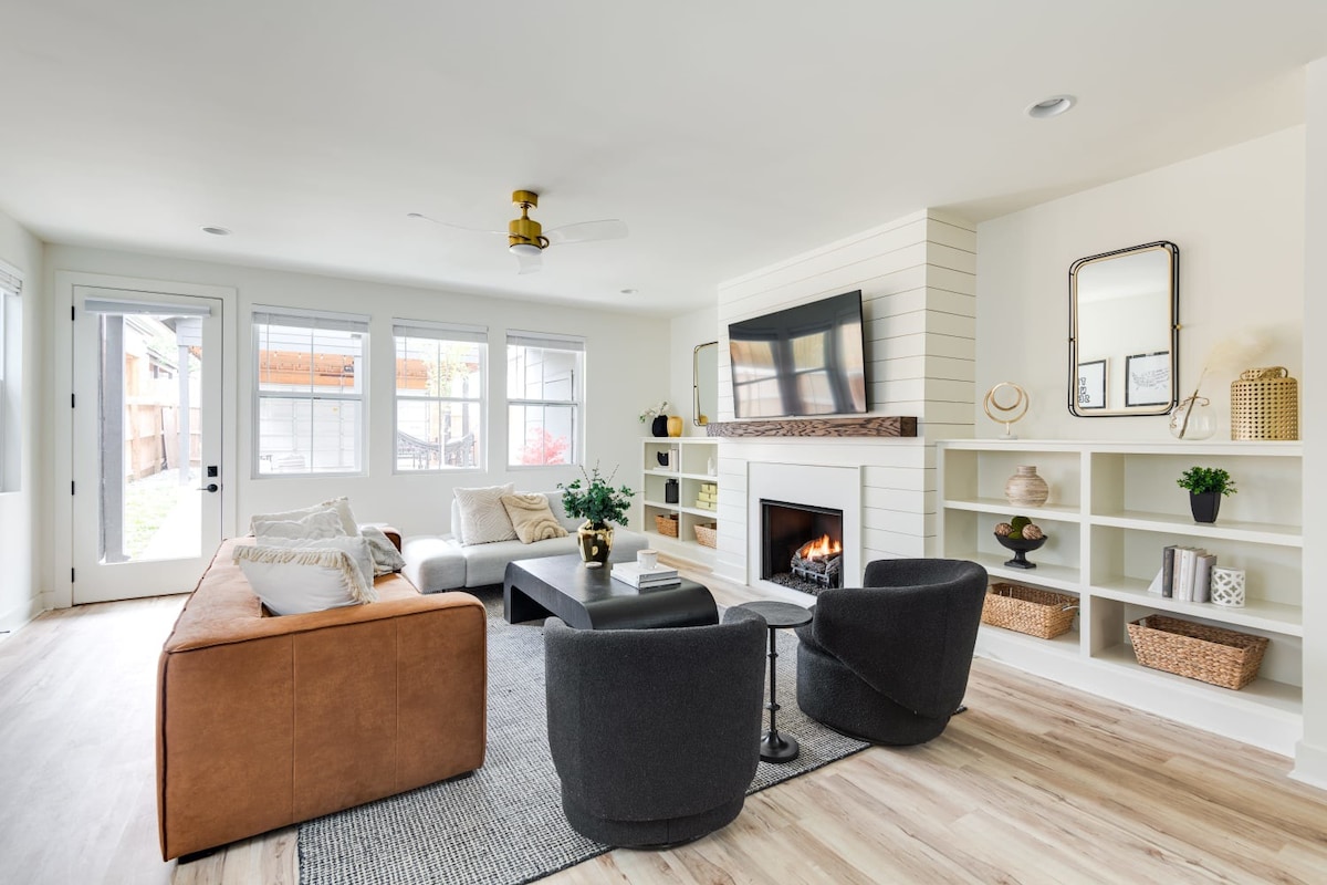 Spacious living room with a brown leather sofa, a light gray sofa, two dark gray swivel chairs, a black coffee table, and a fireplace with a TV mounted above, flanked by white built-in shelves.