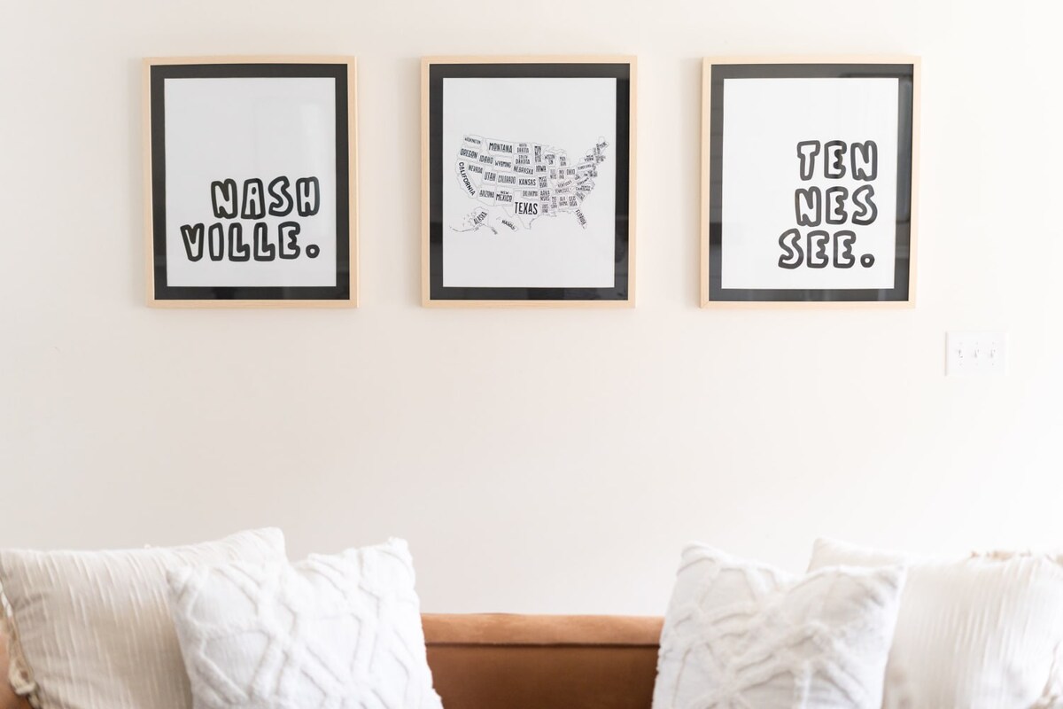 Close-up of three framed art pieces on a light wall above a sofa, featuring 'NASHVILLE.', a map of the US with states labeled, and 'TEN NES SEE.' in black text, adding a local touch to the decor.