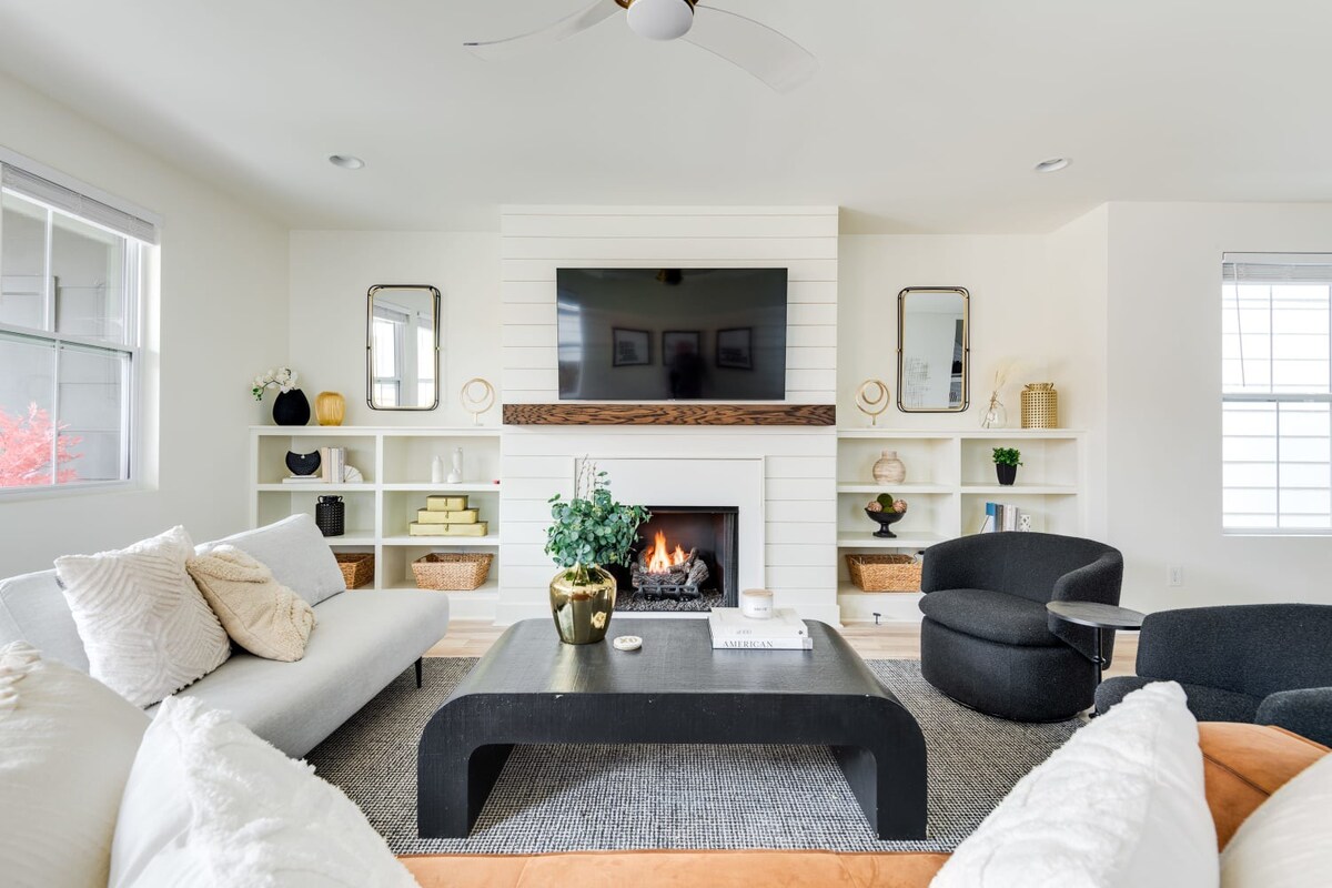 View of the living room from behind the light gray sofa, showing a black coffee table, two dark gray swivel chairs, and a fireplace with a TV mounted above, flanked by white built-in shelves.
