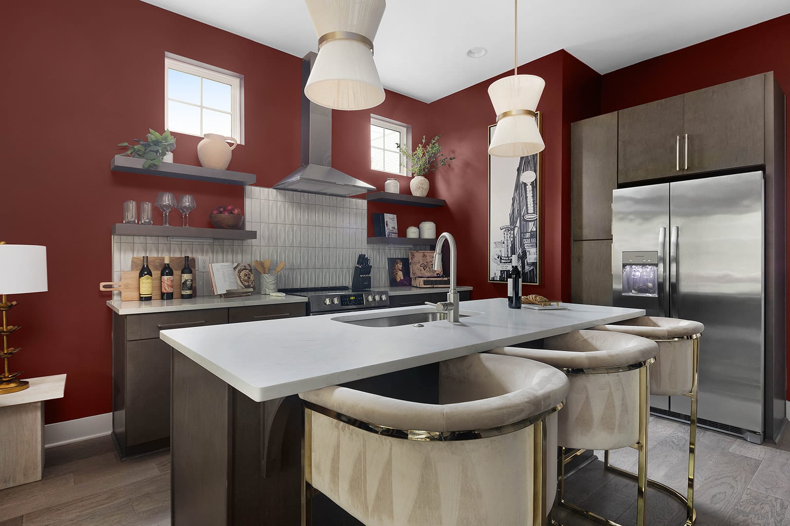 A modern kitchen features bold red walls, dark wood cabinetry, white quartz countertops, a large island with three cream-colored bar stools, and stainless steel appliances.