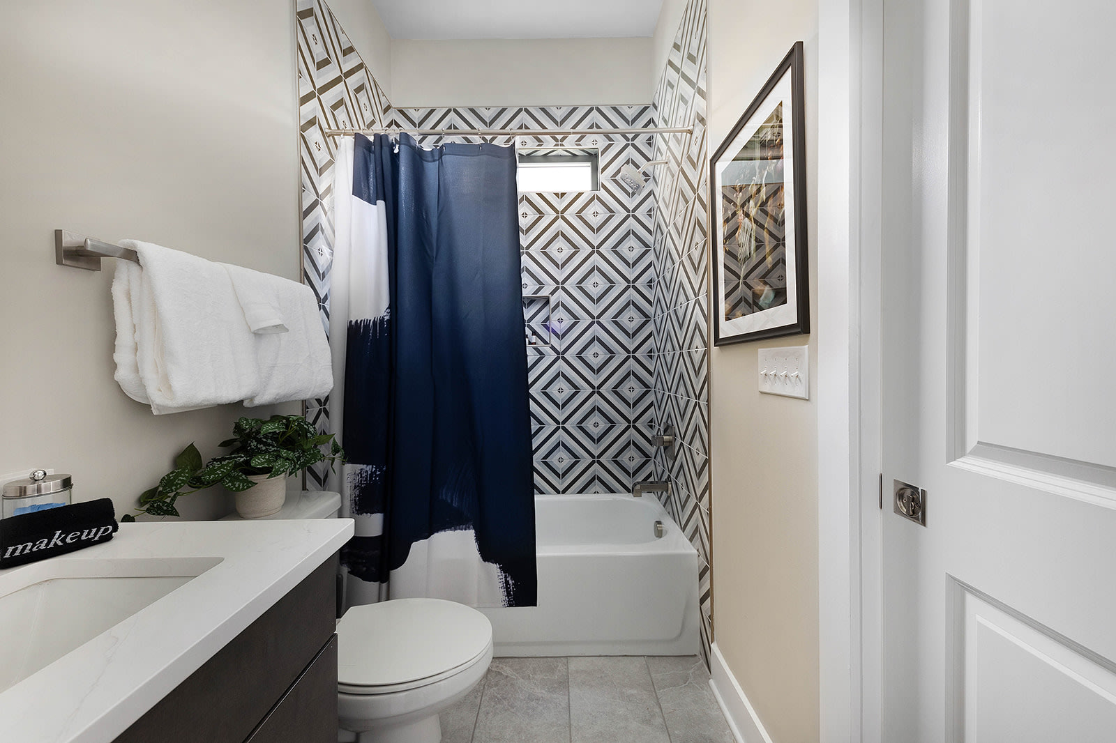 A view of a bathroom's tub and shower area, showcasing a white bathtub against a wall with a bold black and white geometric patterned tile. A dark blue shower curtain is drawn, and a small window is visible above the tub.