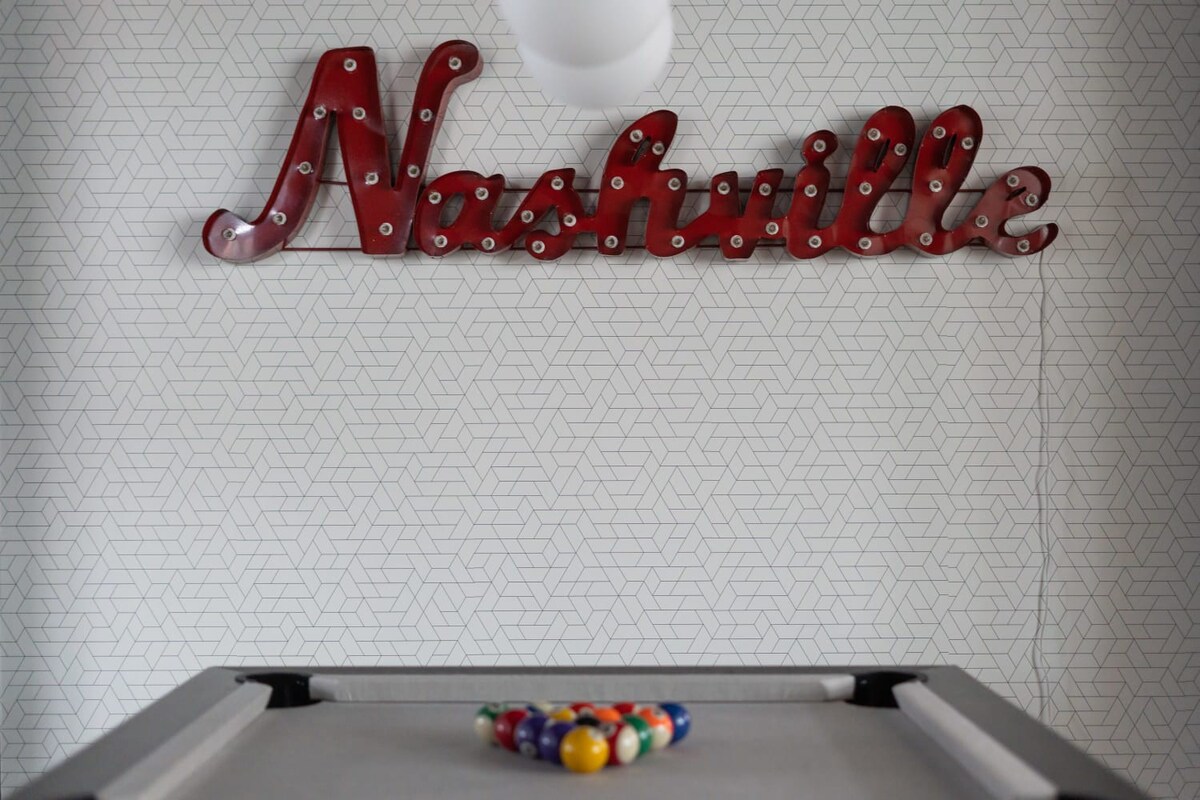 A close-up shot of the "Nashville" marquee sign above the pool table, highlighting the white geometric patterned wallpaper and the colorful pool balls racked on the table.