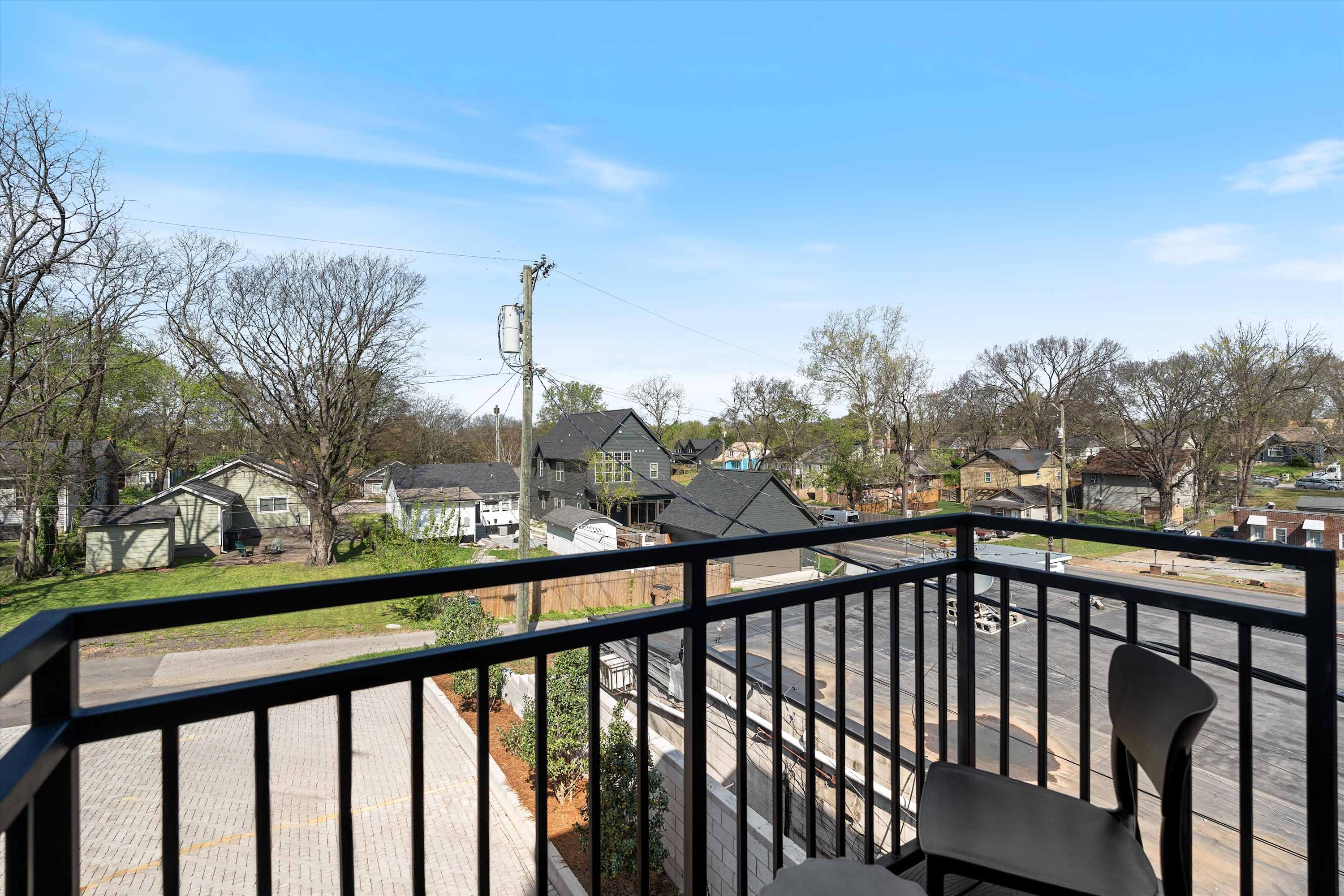 A balcony with black metal railings providing an expansive view of the surrounding neighborhood, including residential homes and mature trees under a clear sky.