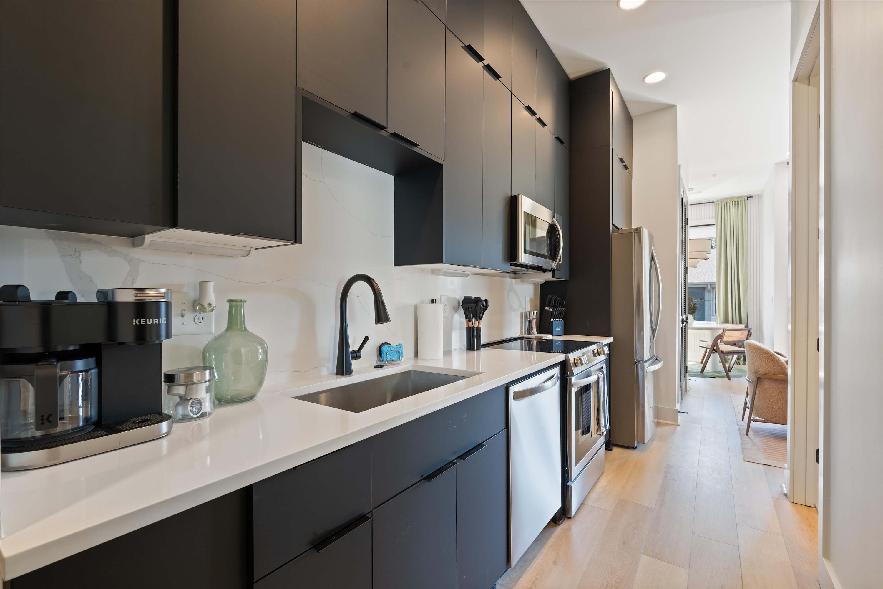 Modern kitchen with dark cabinetry, white quartz countertops, and stainless steel appliances. A Keurig coffee maker and various kitchen essentials are visible on the counter.
