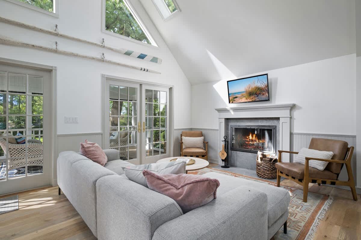 Cozy living room featuring a light grey sectional sofa, a modern fireplace with a grey mantel, and light wood floors, with French doors leading to an outdoor screened porch.