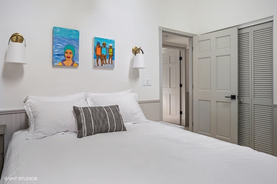 Another perspective of bedroom (Bedroom-2) with a white bed, light gray wainscoting, and vibrant artwork. A closed door and louvered closet doors are visible, maintaining a clean aesthetic.