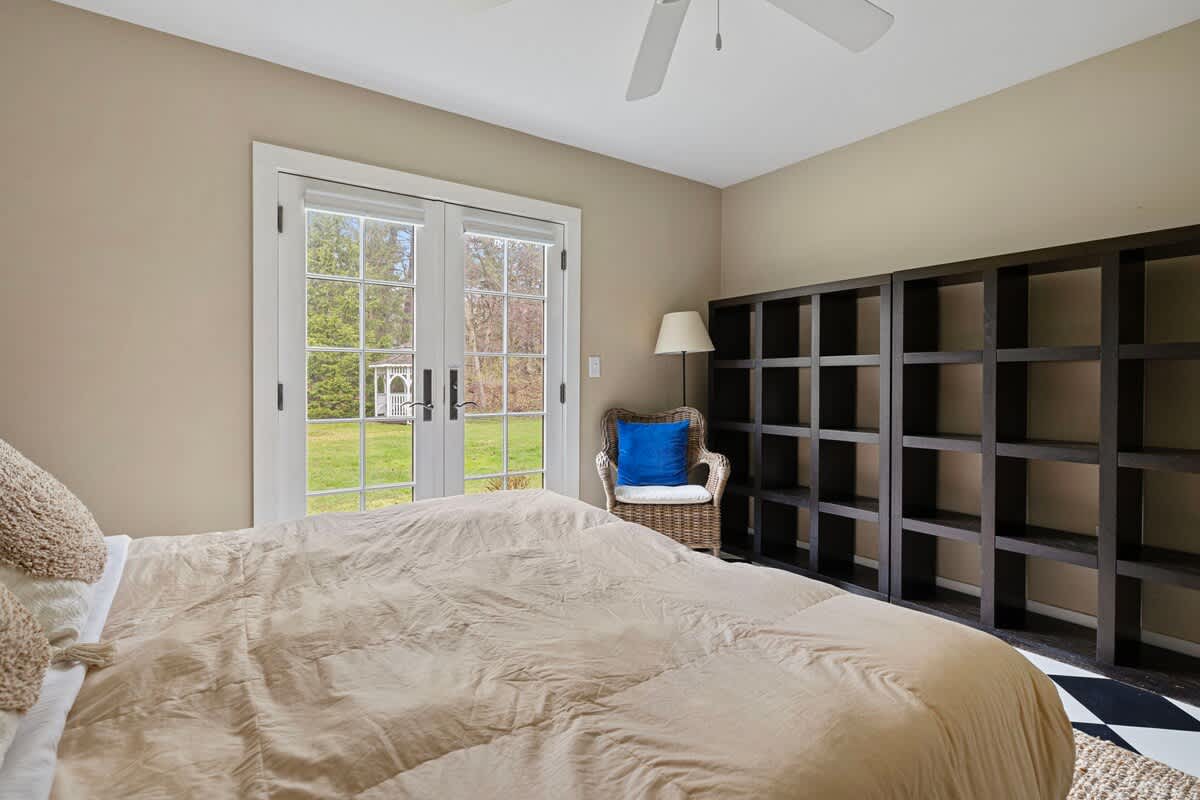Another angle of the bedroom, showing the queen bed, a large black shelving unit, and French doors leading to the exterior. The room has light beige walls and a black and white checkered floor, with a rug under the bed.