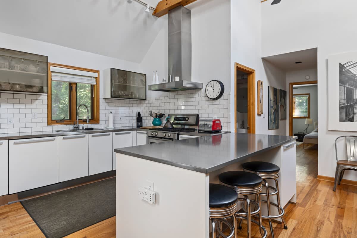 Contemporary kitchen featuring white flat-panel cabinets, stainless steel appliances including a range and hood, subway tile backsplash, and a large island with bar seating, all set on hardwood floors.