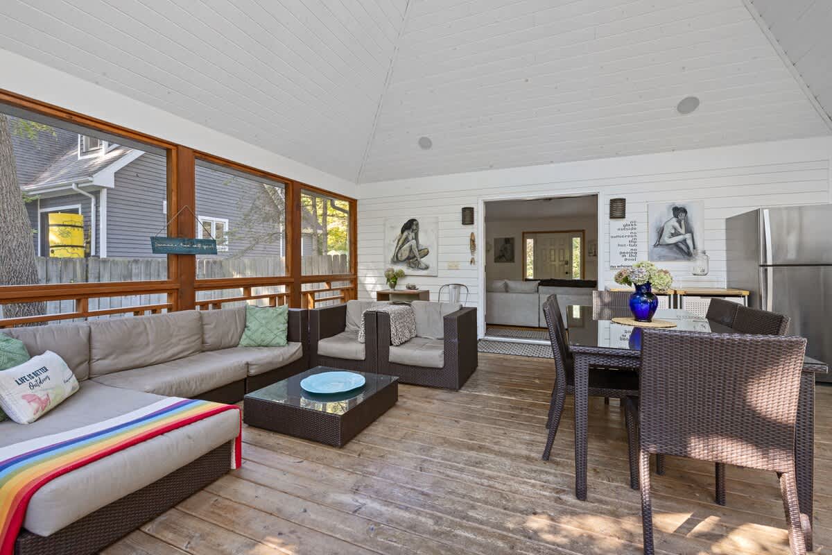 Spacious screened-in porch furnished with a large L-shaped outdoor sofa and armchairs, a coffee table, and a dining set, featuring a vaulted ceiling and wooden deck flooring.