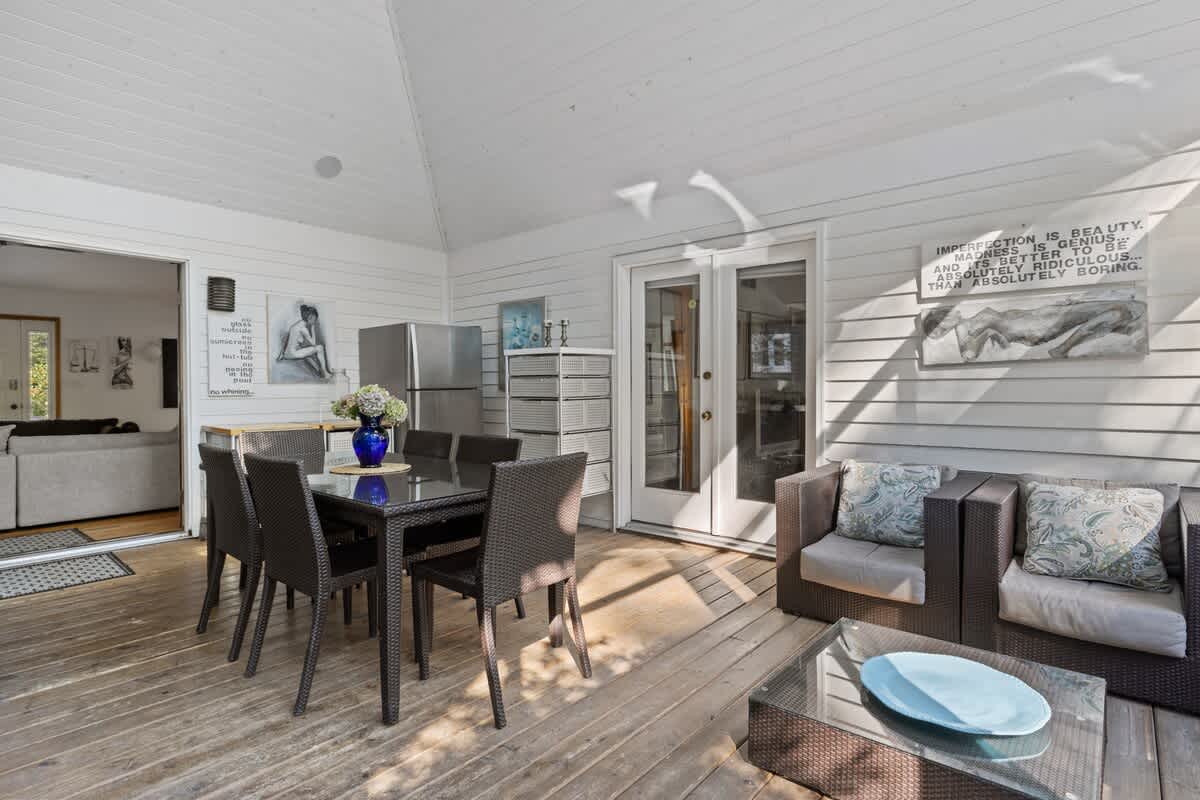 Screened-in porch with a dark wicker dining set and a separate seating area with a sofa and armchairs, featuring white shiplap walls and wooden deck flooring.