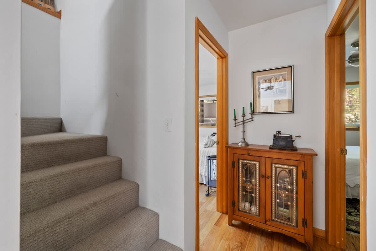 A welcoming foyer area with a carpeted staircase leading upstairs and hardwood floors. A decorative wooden cabinet with glass doors and a candelabra sits against the wall, beneath framed artwork.