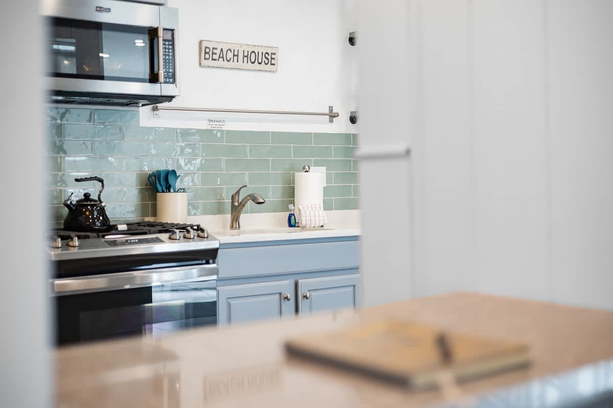 Close-up view of the kitchen counter with a stainless steel gas range, microwave, and sink. The light green subway tile backsplash and light blue cabinets create a fresh, coastal feel.