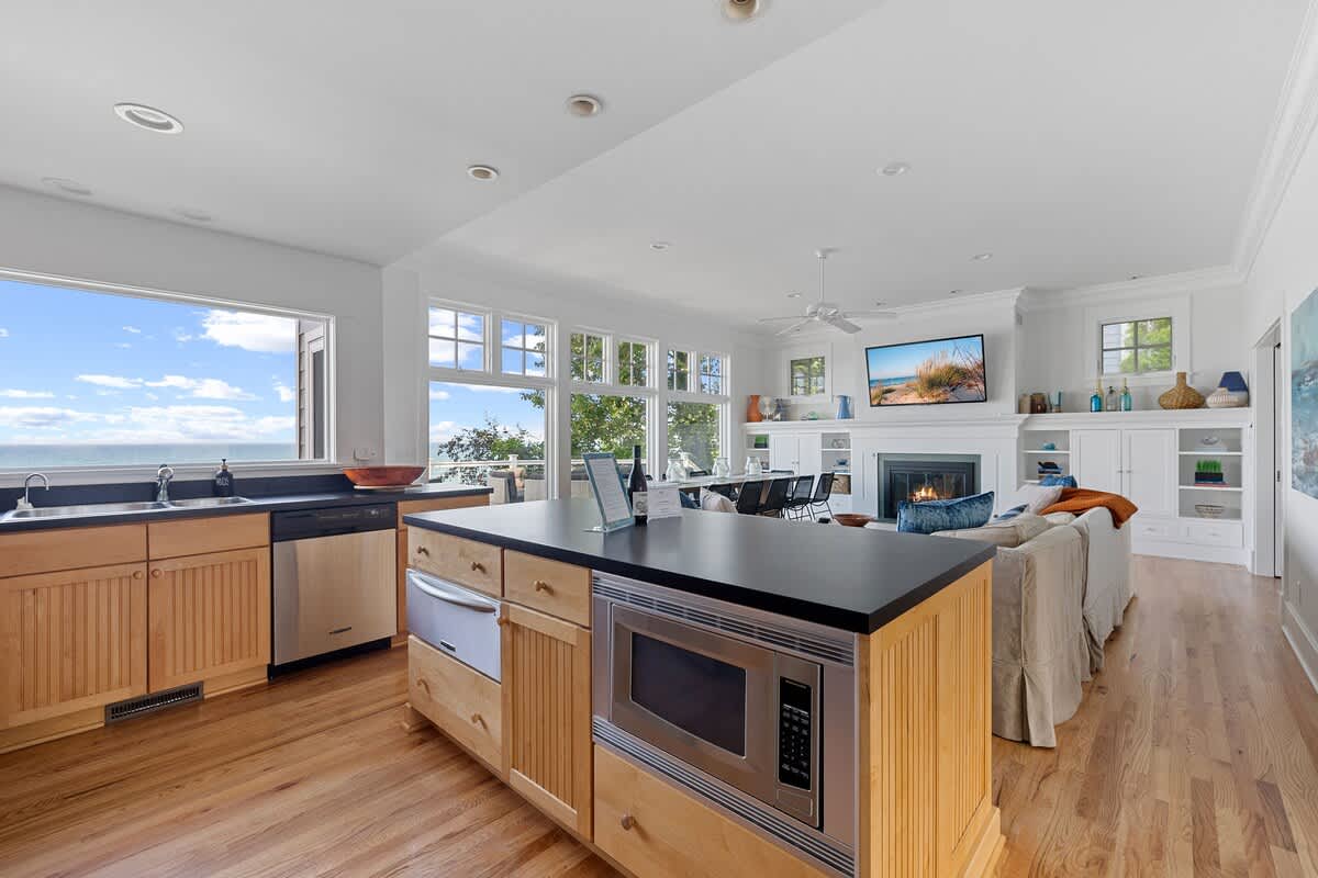 The kitchen island, equipped with a built-in microwave and wine fridge, anchors an open-concept space that extends to the living room and dining area, all boasting stunning lake views through large windows.