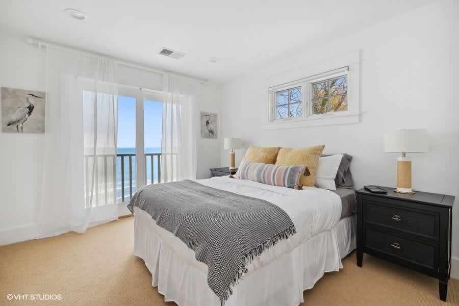 Serene bedroom with a queen-sized bed, dark wooden nightstands, and a private balcony offering direct views of the lake. White sheer curtains frame the glass doors, enhancing the airy feel.