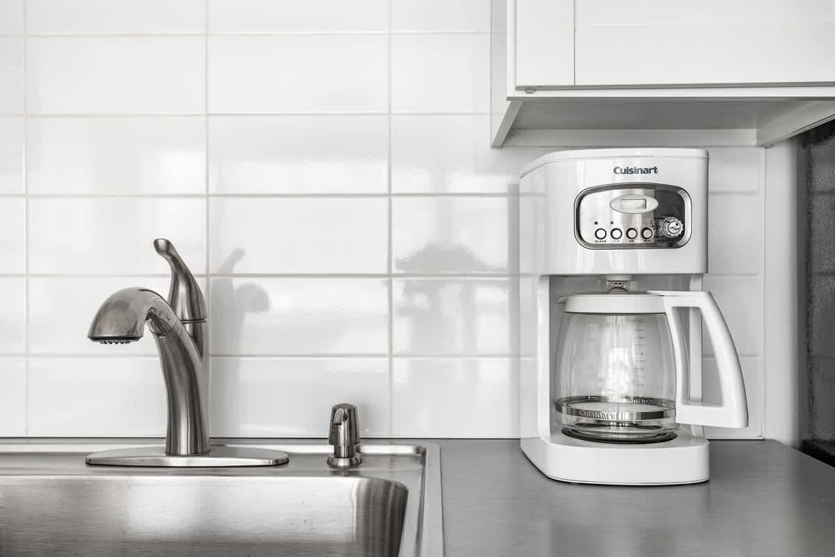 Detail shot of the kitchen sink with a modern chrome faucet and a white Cuisinart coffee maker on the light gray countertop, backed by white subway tiles.