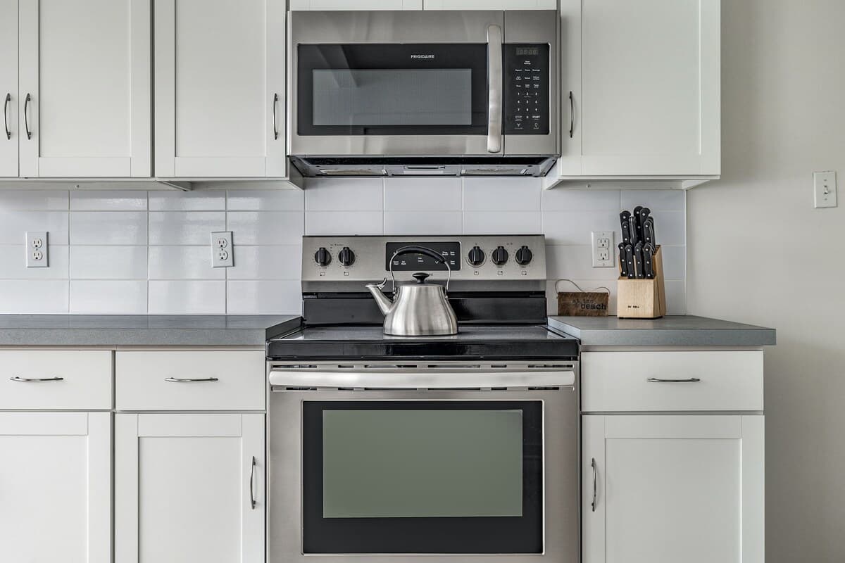 Close-up view of the kitchen's stainless steel electric range with an overhead microwave, set against a white subway tile backsplash and light gray countertops.
