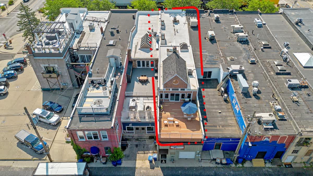 Aerial view showcasing the property (outlined in red) as part of a commercial strip, with multiple rooftops, adjacent buildings, and surrounding urban infrastructure.