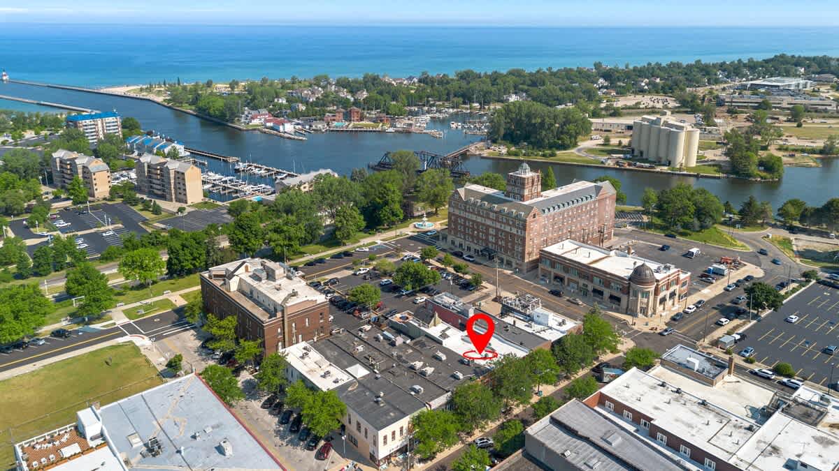 Wide aerial view of the property's location (marked with a red pin) within a town, showing its proximity to a large body of water, a harbor, and surrounding urban landscape.