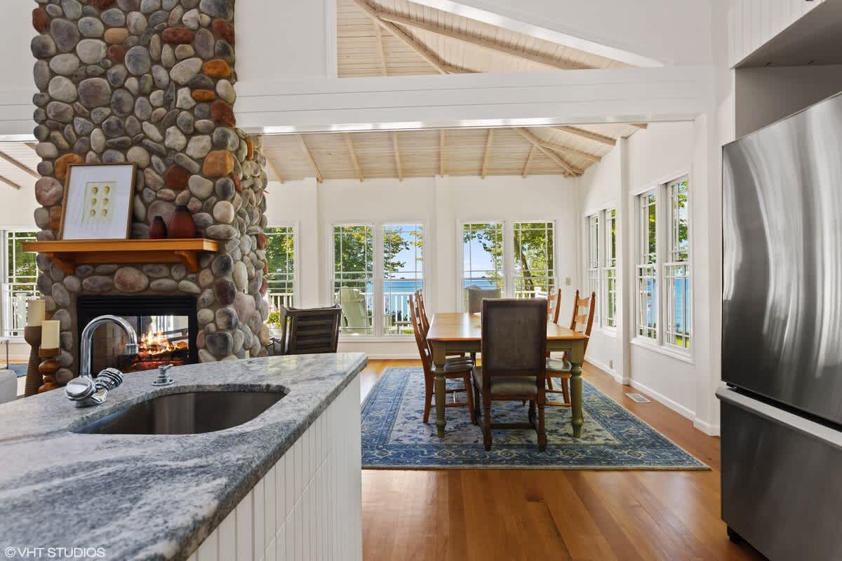 View from the kitchen island, highlighting the granite countertops and sink, looking towards the dining area with a large stone fireplace and windows offering a bright lake view.