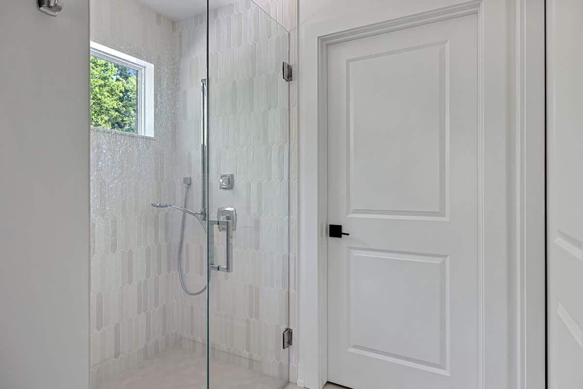 Modern bathroom shower with light-colored vertical subway tiles, a glass enclosure, and a small window providing natural light.