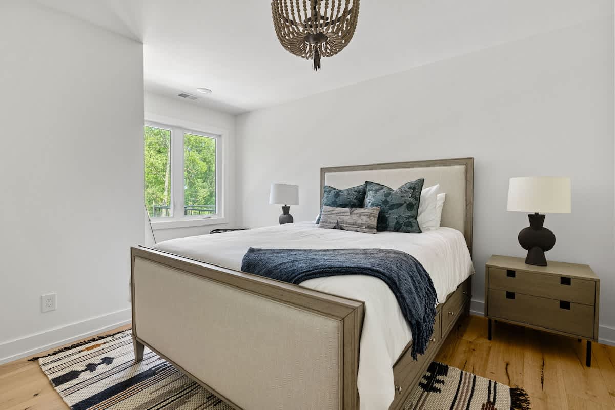 Bright bedroom-1 featuring a large bed with a light upholstered frame, a decorative chandelier, and large windows overlooking lush greenery.