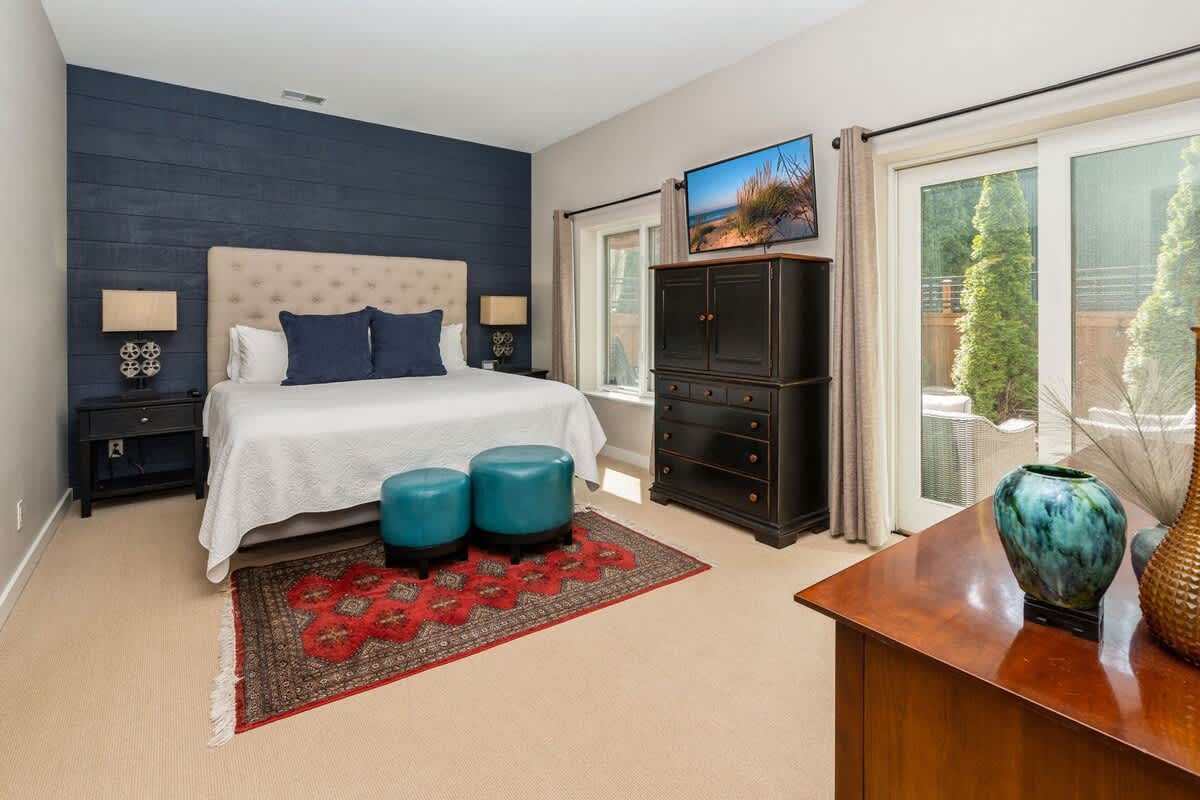 Cozy bedroom with a tufted headboard bed, navy accent wall, dark wood dresser with a TV, and a sliding glass door leading to an outdoor patio.