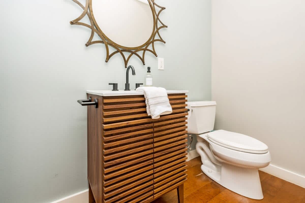 Chic powder room with a unique slatted wood vanity, a sunburst mirror, and a white toilet, set against a light blue wall.