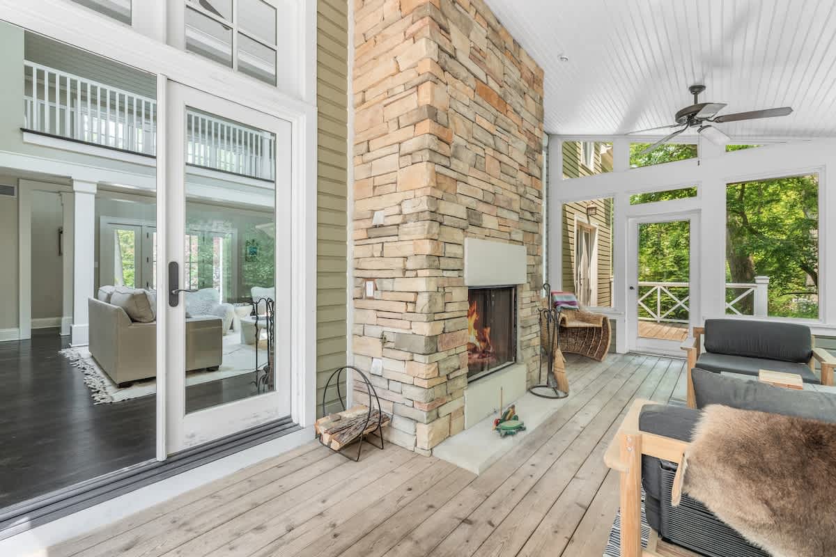Inviting screened porch with a prominent stone fireplace, comfortable seating including a sofa and armchairs, and glass sliding doors connecting to an interior living space.