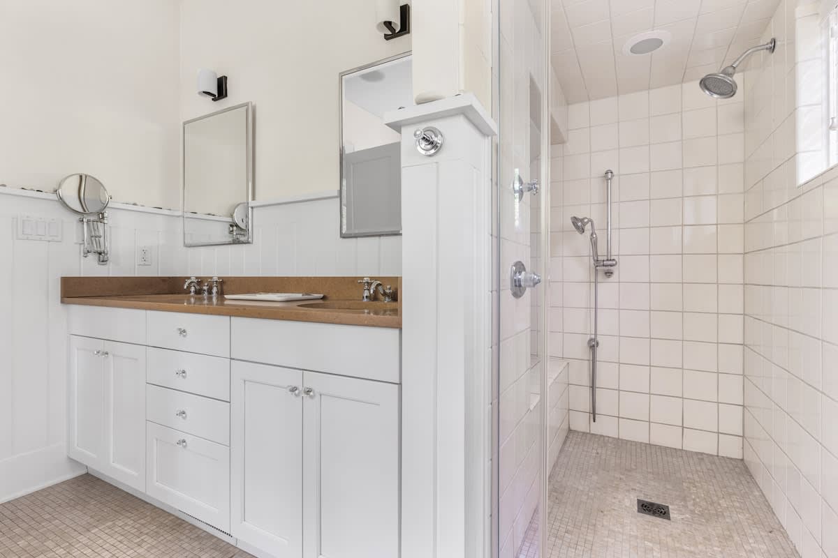 A modern bathroom featuring a walk-in shower with white subway tiles and a glass door, adjacent to a double vanity with white cabinets and a light brown countertop.