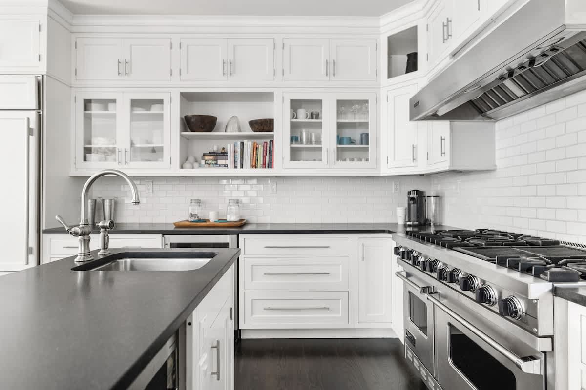 Spacious white kitchen featuring extensive cabinetry, dark countertops, a large stainless steel range with a hood, and a subway tile backsplash, with a sink visible on the island.