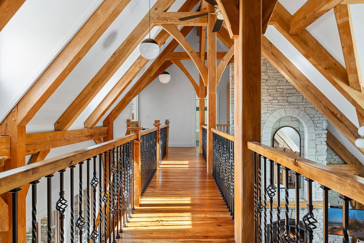 Architectural interior featuring a wooden walkway or bridge on an upper level, with ornate black metal railings and exposed wooden beams forming a striking vaulted ceiling. Spherical pendant lights illuminate the space.