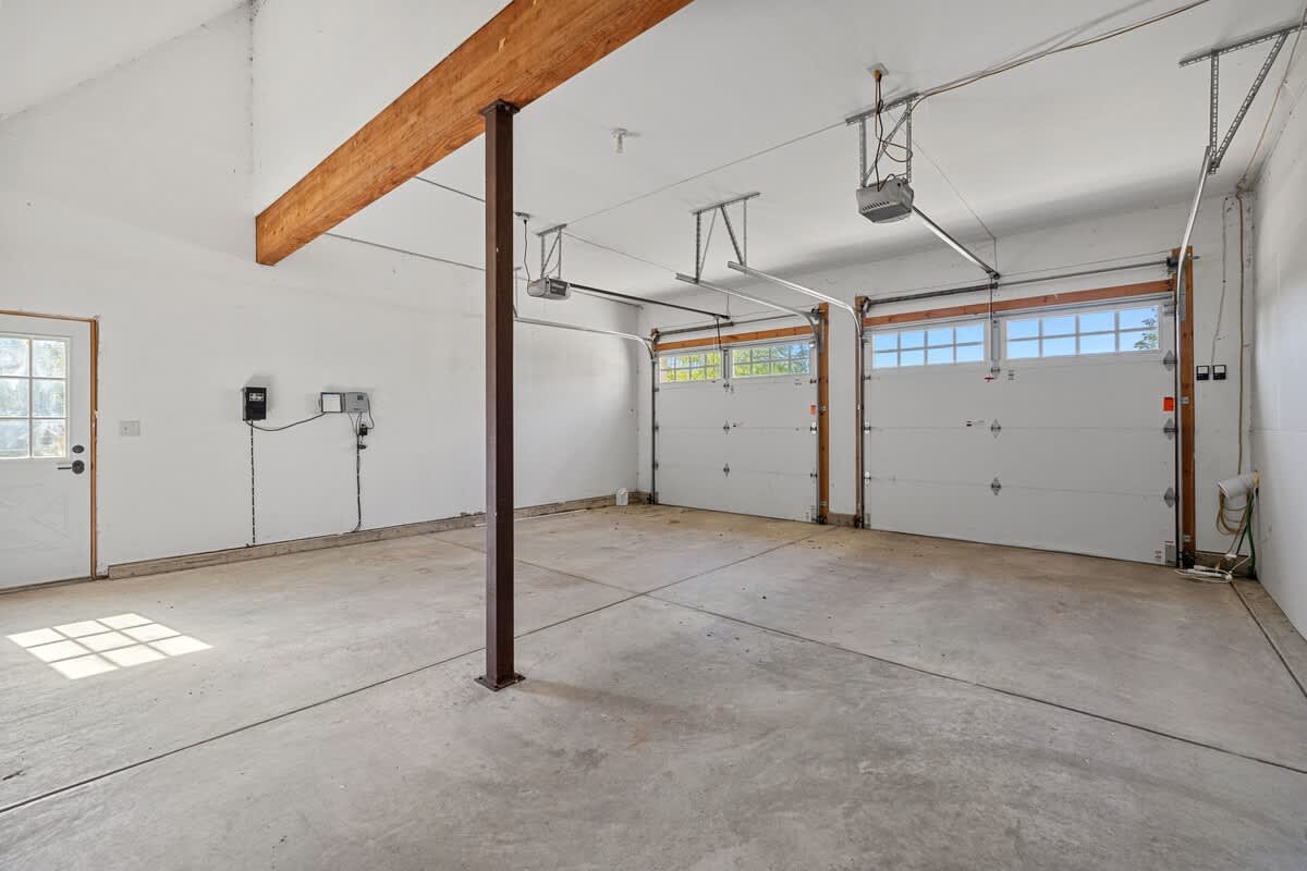 A bright, spacious two-car garage with white walls and a concrete floor features two white garage doors with windows, an exposed wooden beam, and a central support post.