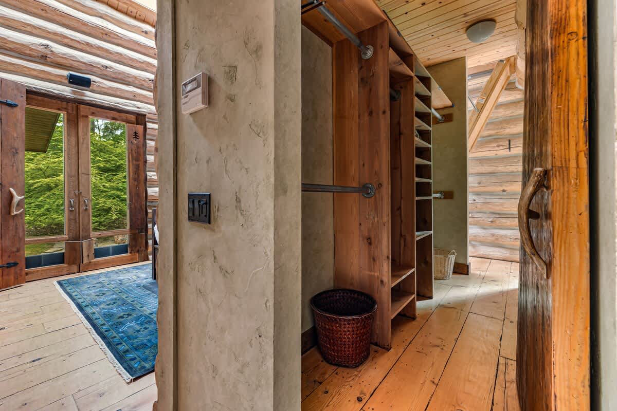 Rustic hallway or dressing area with log cabin walls and wooden floors, featuring a built-in wooden closet with shelving and hanging space, adjacent to glass double doors leading outdoors.