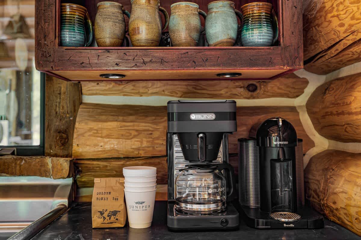 A dedicated coffee station in the kitchen, equipped with a drip coffee maker, a single-serve coffee machine, and ceramic mugs on an open shelf above.