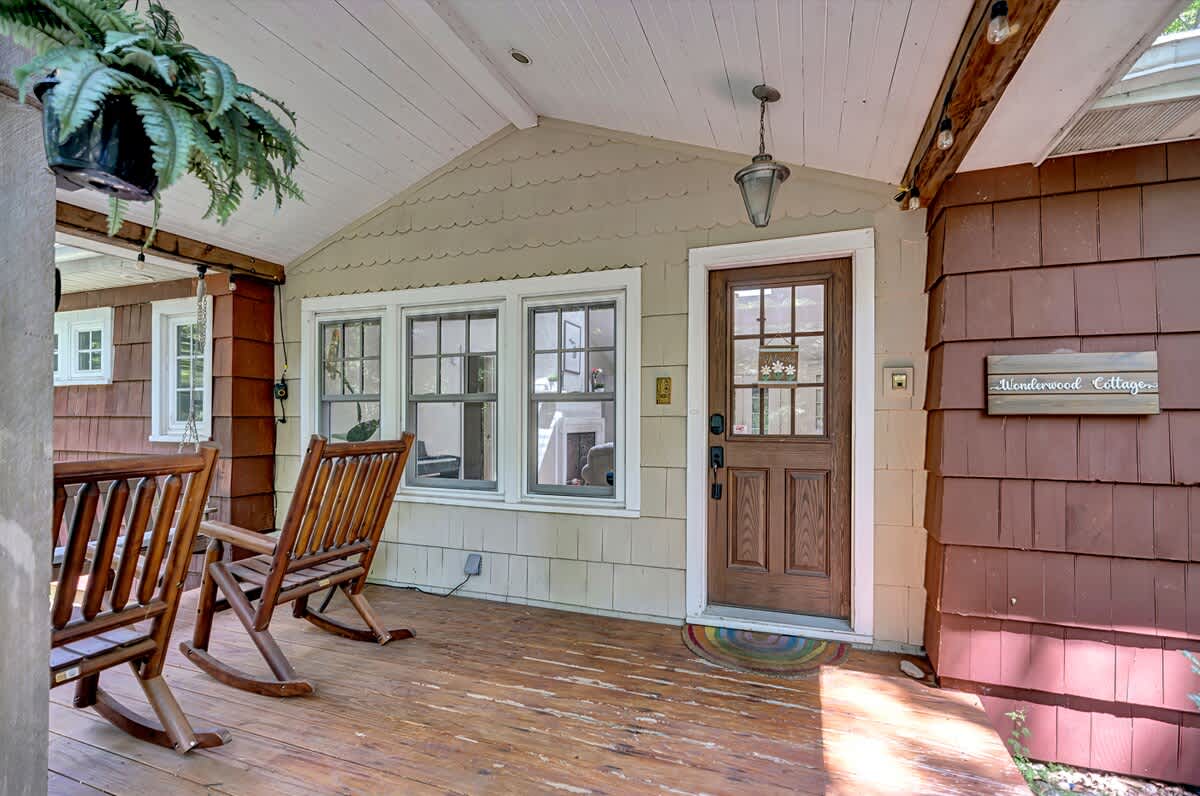 Welcoming front porch with a wooden floor and two classic wooden rocking chairs. The front door features glass panels, and a "Wonderwood Cottage" sign is mounted on the wall.