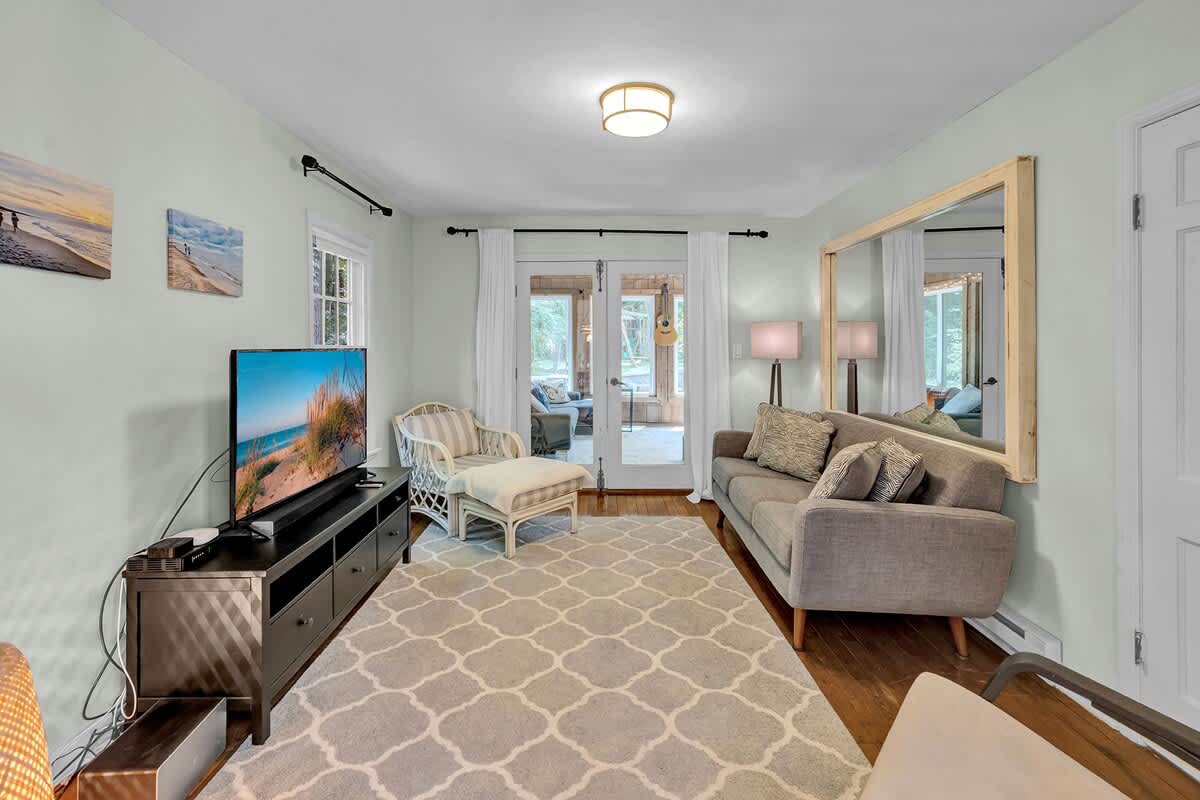 Relaxing living area with light blue walls, a gray sofa, and a wicker armchair. A large mirror reflects the room, and French doors lead to an adjacent sunroom.