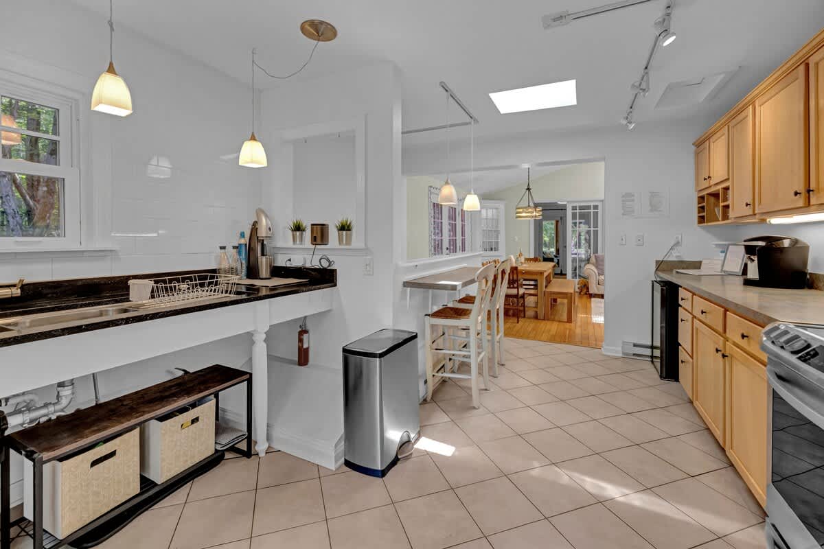 A spacious kitchen with light wood cabinetry and tiled floors, featuring a breakfast bar with seating, a large sink area, and a skylight for natural light.