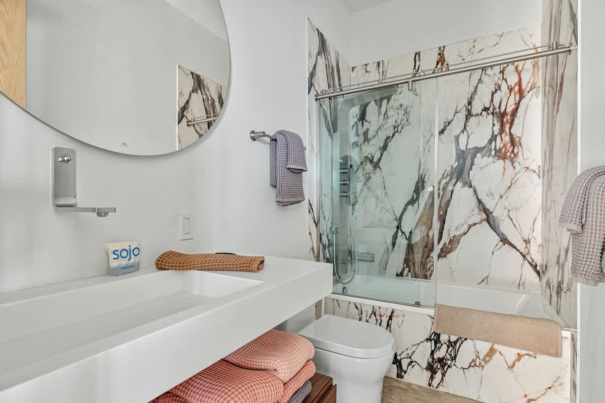 Modern bathroom with a white floating vanity, round mirror, and a bathtub/shower combo featuring striking white and brown marble-patterned wall tiles.