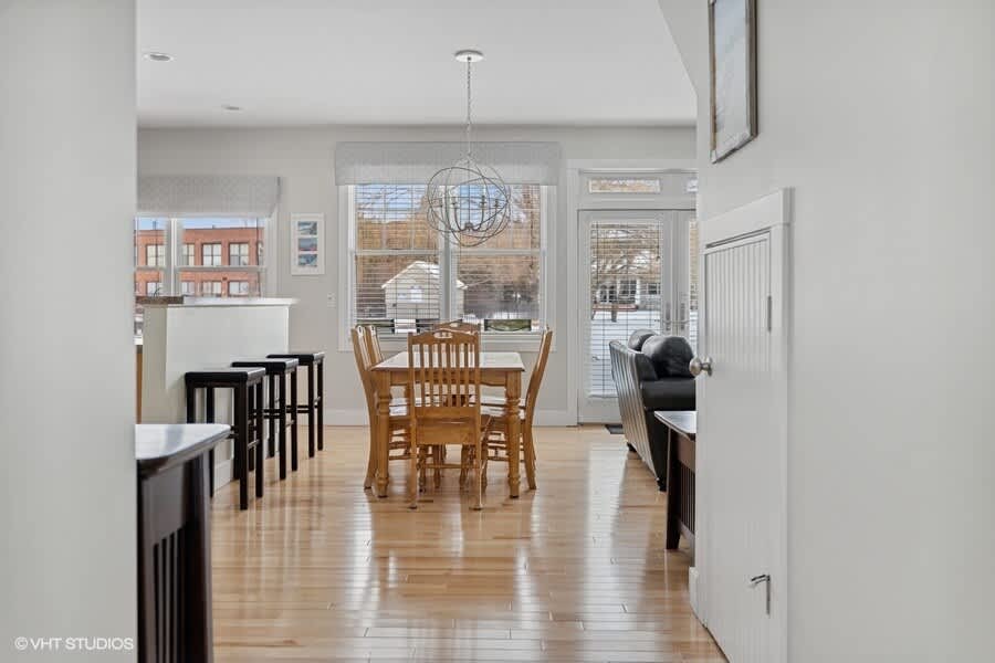 Open-concept dining area with light hardwood floors, a wooden dining table with six chairs, and a modern spherical chandelier, seamlessly connecting to the living room and kitchen areas.