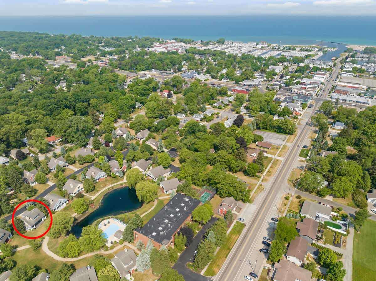 A broad aerial view showcases the entire community, with the property circled, nestled among trees and residential areas. A large body of water with a marina is visible in the distance under a partly cloudy sky.