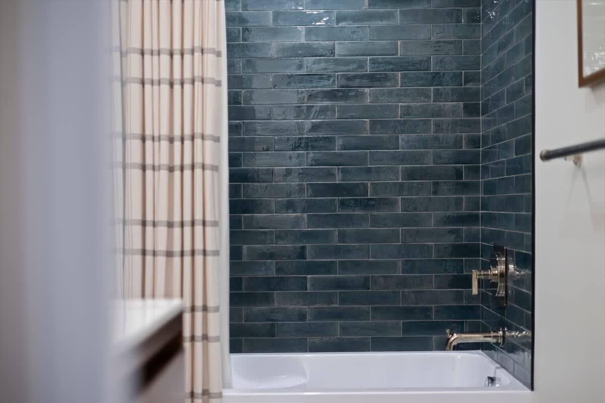 Close-up of a bathtub/shower combo with glossy dark blue subway tiles arranged horizontally. The shower curtain is striped, and chrome fixtures are visible.