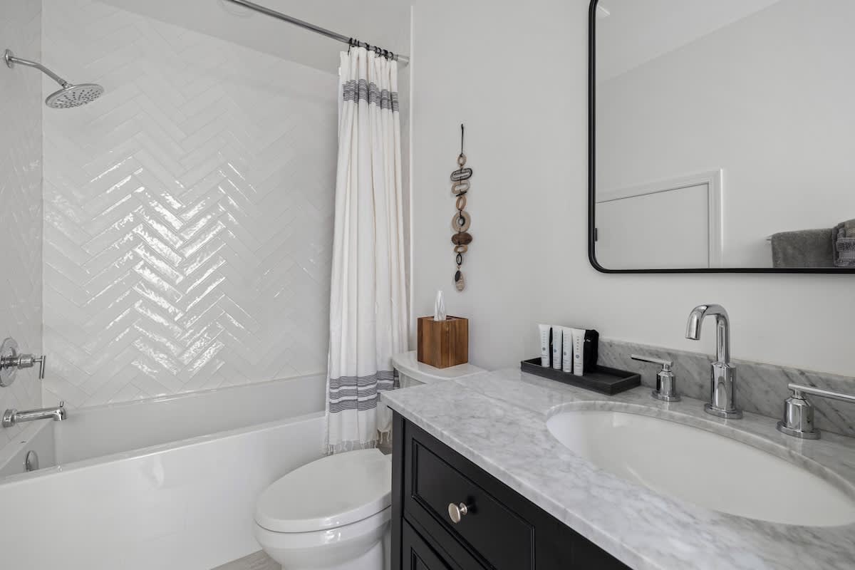 A modern bathroom featuring a white subway tile shower/tub combo in a herringbone pattern, a dark vanity with a marble countertop and oval sink, and a large rectangular mirror.