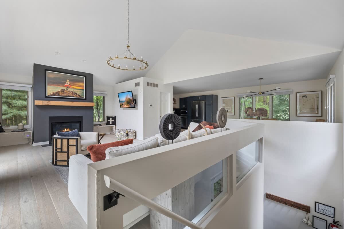 An elevated view of the open-concept living space shows a large sectional sofa facing a fireplace with artwork above, a modern chandelier, and an adjacent kitchen area visible in the background.