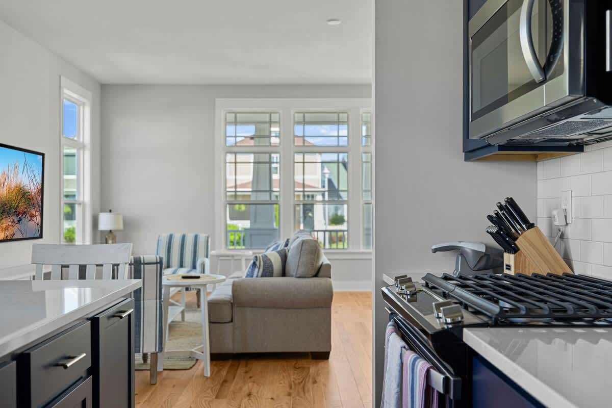 Modern kitchen with dark blue lower cabinets, white subway tile backsplash, and stainless steel appliances, including a gas range and microwave, with a view into the living room.