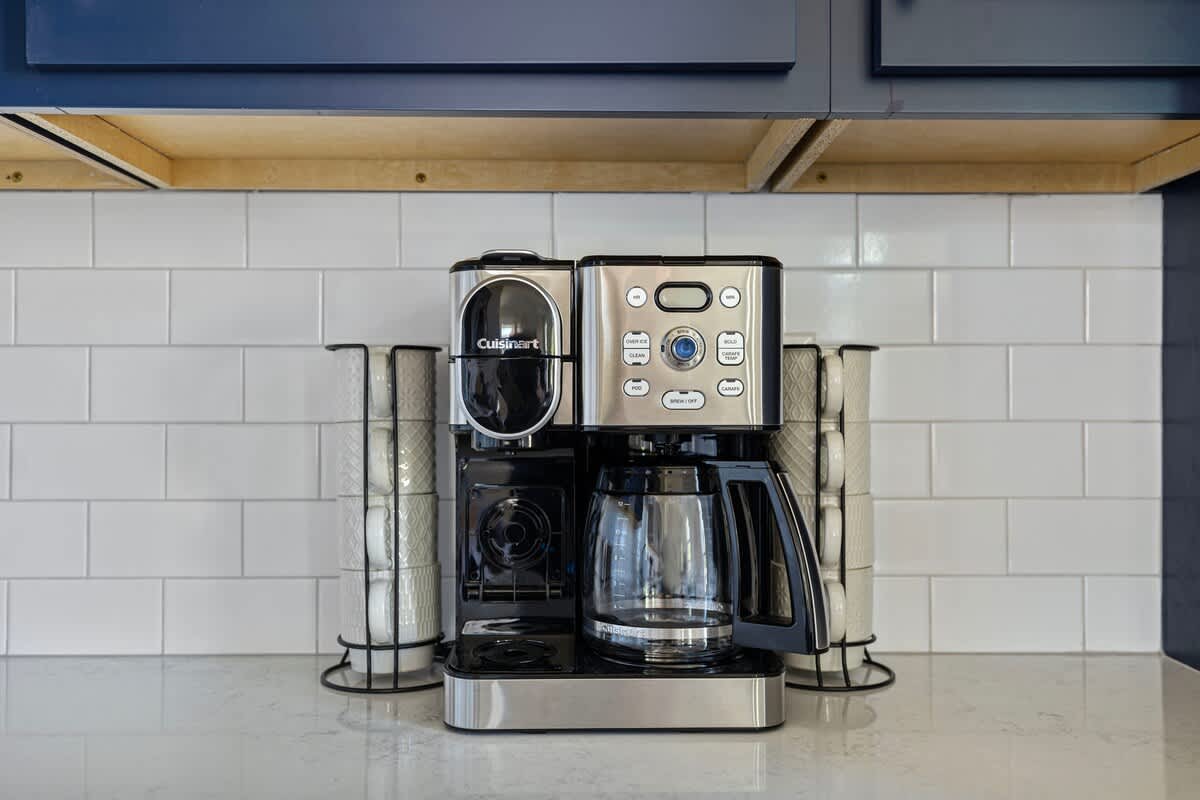 Close-up of a Cuisinart coffee maker on a white quartz countertop, set against a white subway tile backsplash, with dark blue upper cabinets visible above.