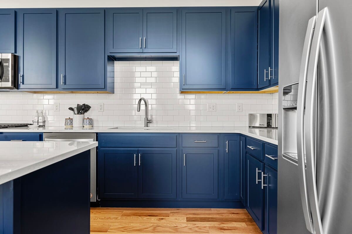 Detailed view of the kitchen's dark blue shaker cabinets, white subway tile backsplash, and white quartz countertops, complete with a stainless steel sink and modern faucet.